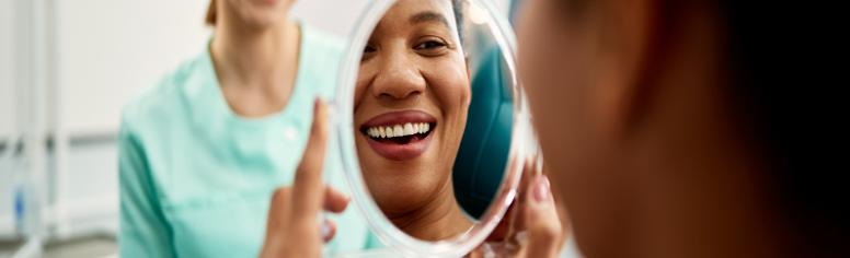 Woman in dentist office looking at her clean teeth in a mirror