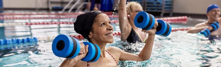 Black woman with group of other older adults doing water aerobics in pool.