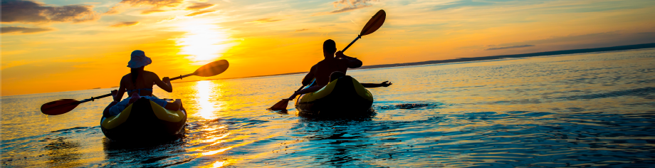 A woman and man kayaking on the ocean at sunset