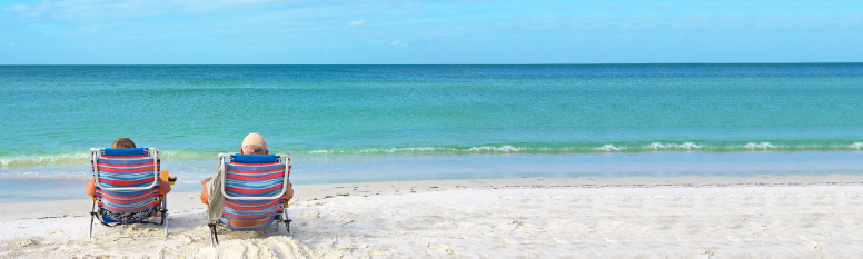 A retired couple sitting in beach chairs on the sand overlooking the ocean